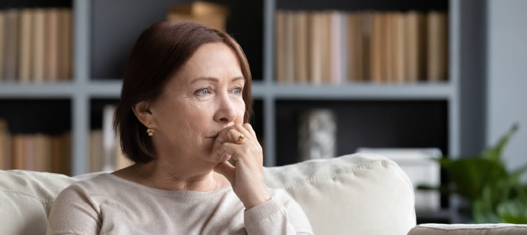 Middle-aged brunette woman seated on a white couch mourning a loved one's wrongful death.