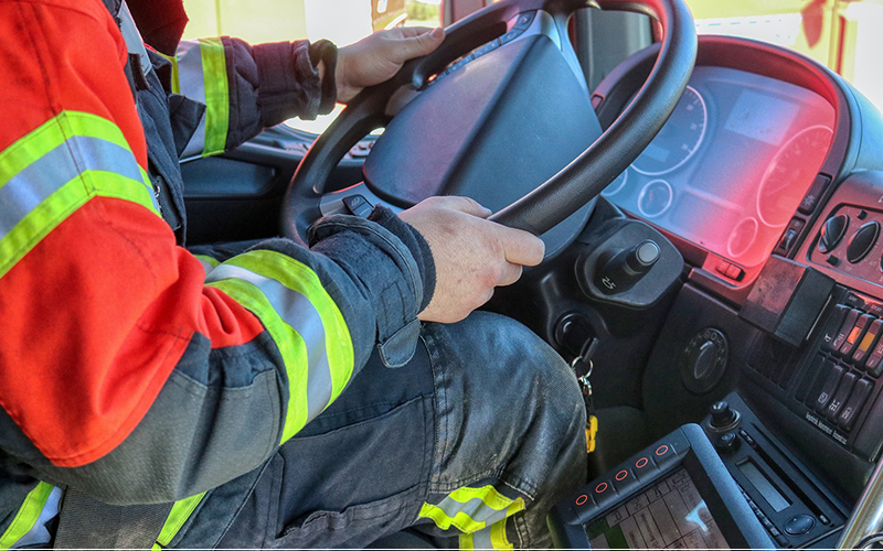 A truck driver in the cab holding the large steering wheel of his vehicle.