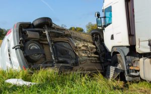 A serious crash involving a semi truck, with a flipped over van in the grass.