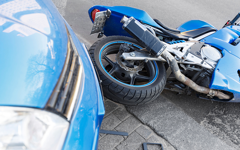 A blue car and motorcycle on the asphalt after a wreck.