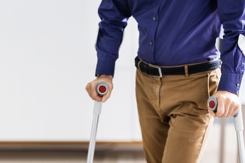 A man in a blue shirt walking using a pair of crutches.