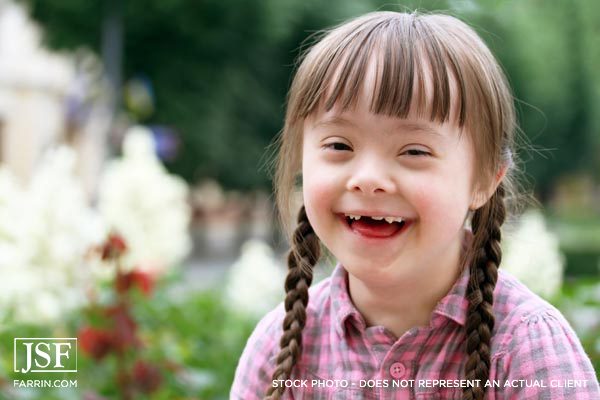 smiling child outside with double braids and Downs Syndrome