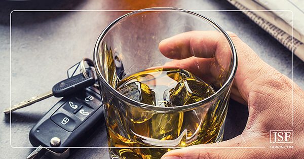 A hand grabbing a glass of whiskey next to car keys, representing drunk driving.