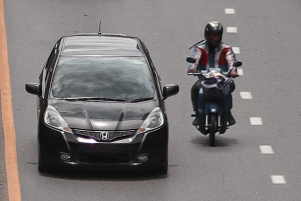 A motorcyclist and a car in the same lane on a gray road.
