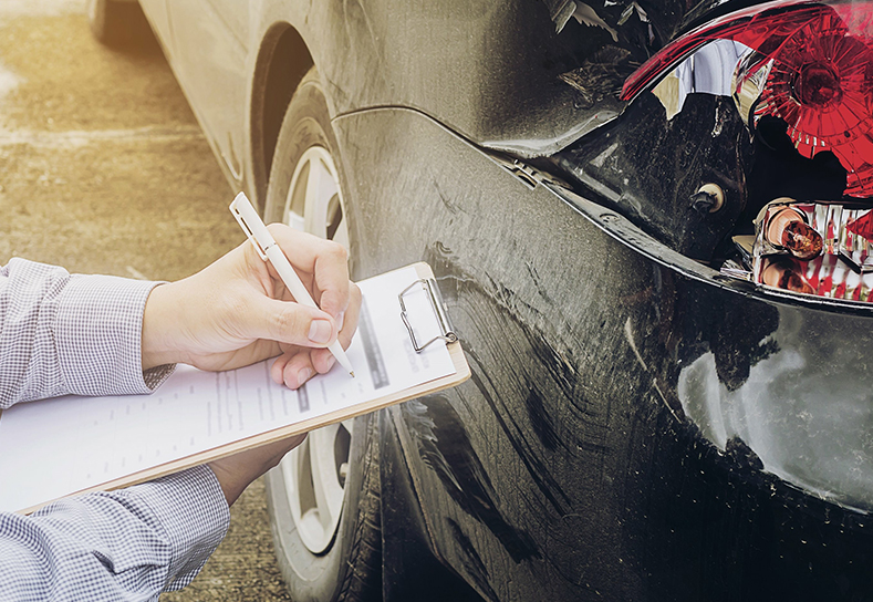 An insurance adjuster taking notes on a clipboard near a black car.