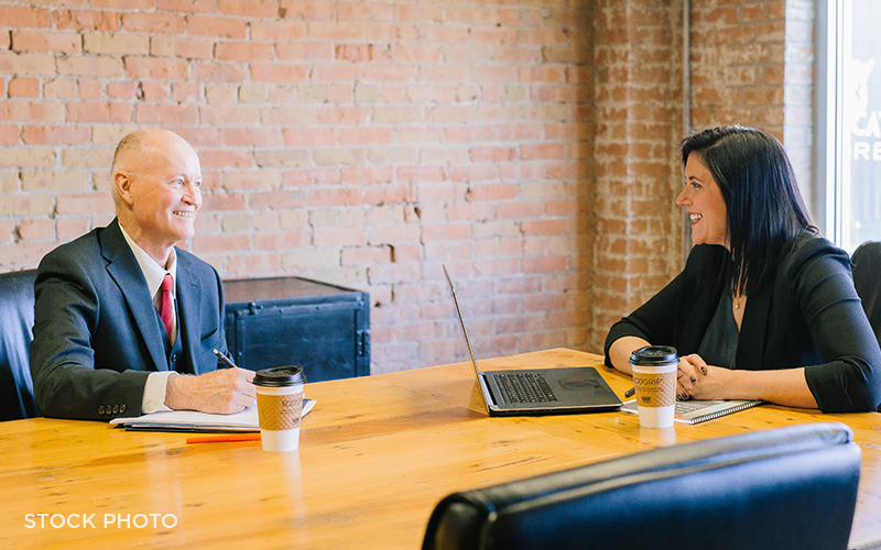 An attorney and a paralegal having a discussion in a meeting room in an office with brick walls.