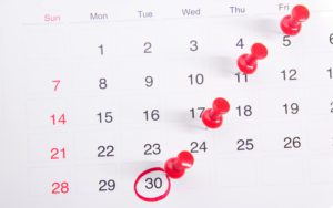 Red thumbtacks on a calendar counting up to day 30.