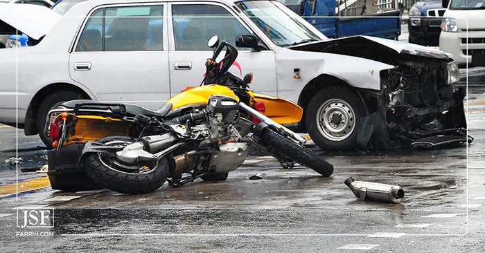 Aftermath of a head-on collision between a yellow motorcycle and a car on the street.