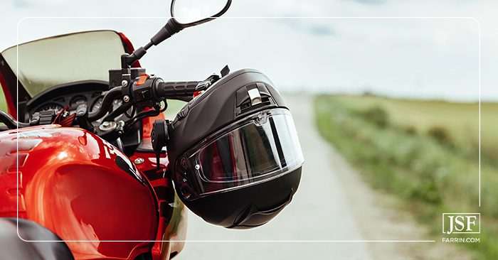A black helmet with visor hanging from the handlebar of a red motorcycle on a road.