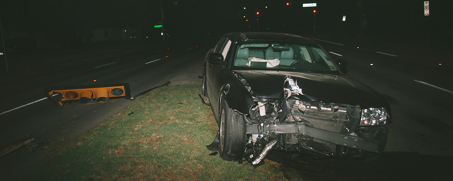 Black car crashed on the side of the road at night.