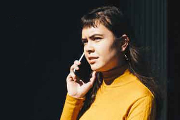 Woman in yellow talking on a cell phone outdoors.