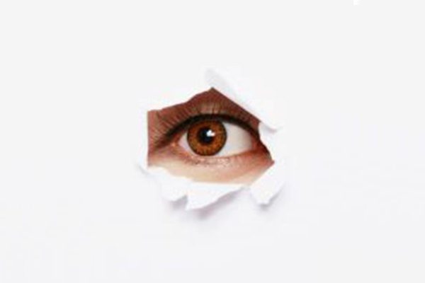Someone's eye peeking through a torn hole in order to spy.
