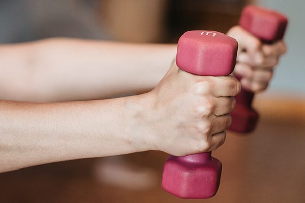 Person holding two red weights during physical therapy.