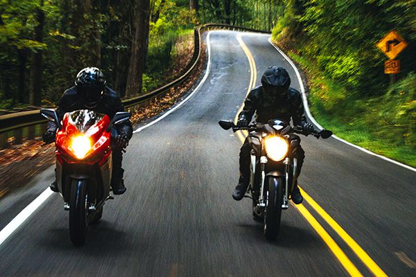 Two motorcyclists on a dark and narrow forest road.