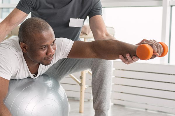Black man working with a physical therapist with weights.