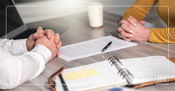 A business man and woman with clasped hands negotiating paperwork in an office.