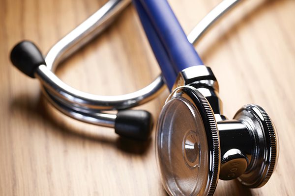 Blue and silver doctor's stethoscope on a wooden desk.