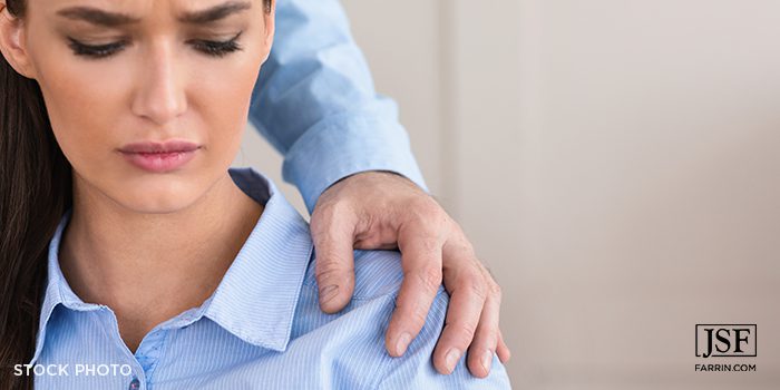 A woman being sexually harassed at work by a supervisor placing his hand on her shoulder.