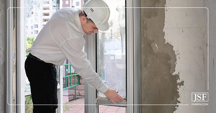 Insurance adjuster in a white hard hat inspecting a water damaged wall in a house.