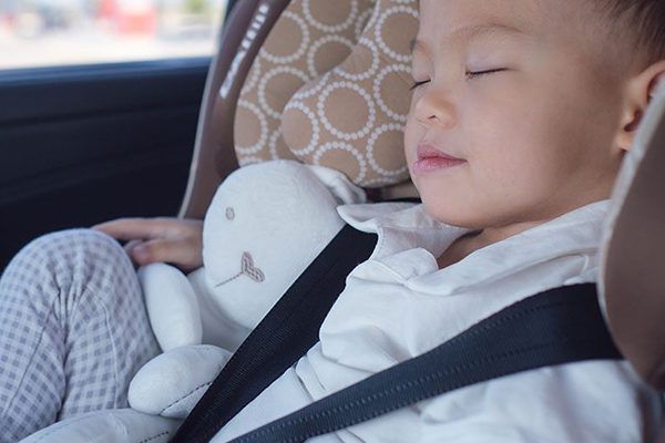 Young boy sleeping in his car seat in the back of a car.