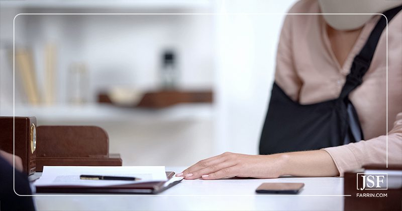 An injured worker with a neck brace & arm sling at a desk with paperwork.