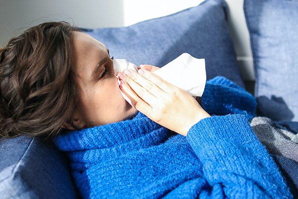 Sick woman in a blue robe with a cold blowing her nose.