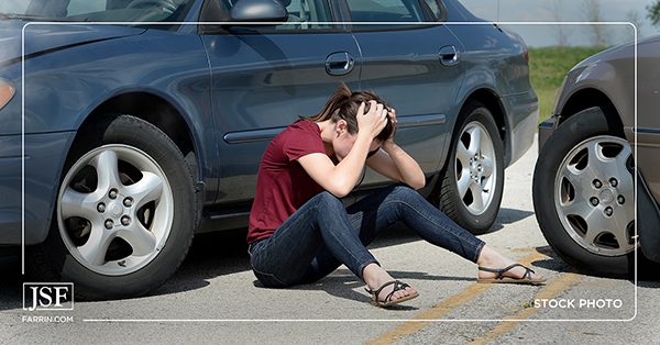 A scared teen girl sitting on the road after a car crash.