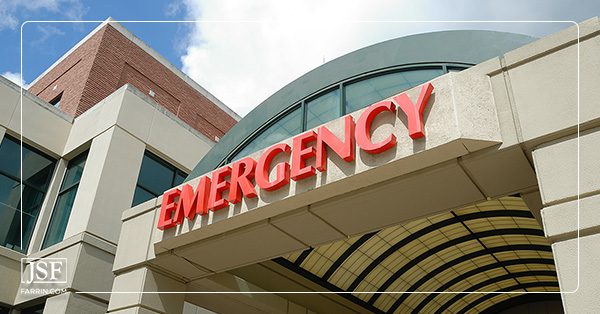 Red EMERGENCY sign marks the exterior of the green domed entrance of a beige stone hospital