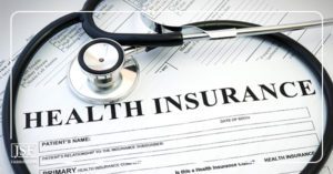 A black stethoscope sits on top of health insurance application forms spread over a white table top