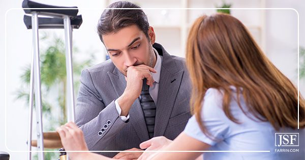 Woman with crutches presents her Workers’ Compensation denial letter to a lawyer in a gray suit