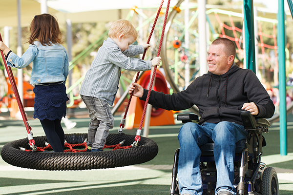 Disabled father in a wheelchair playing with his young children at a playground.