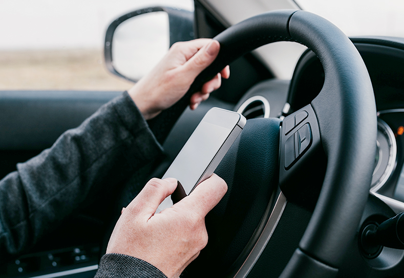 Driver looking at their cell phone over their steering wheel while in a car.