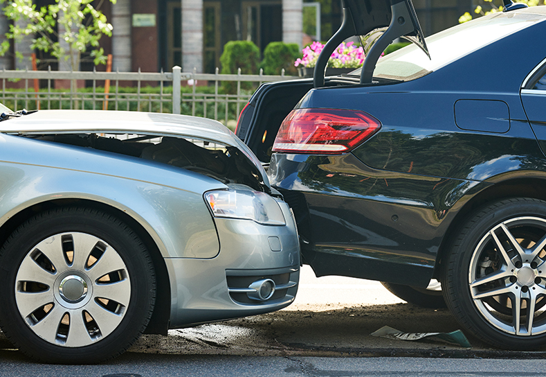 A silver car rear ends and wrecks a black car.