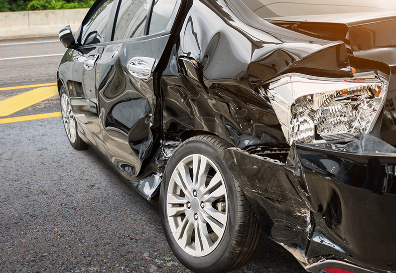 Crumpled side of a totaled black car on the road.