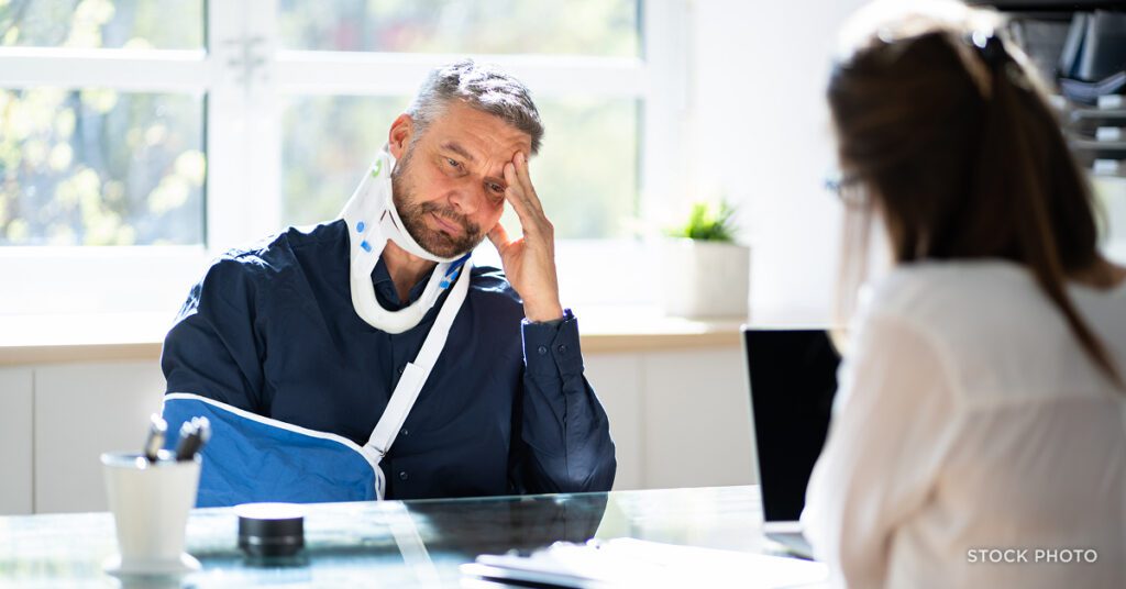Law Offices of James Scott Farrin North Carolina auto accident lawyer consults with injured man showing neck & arm injuries.