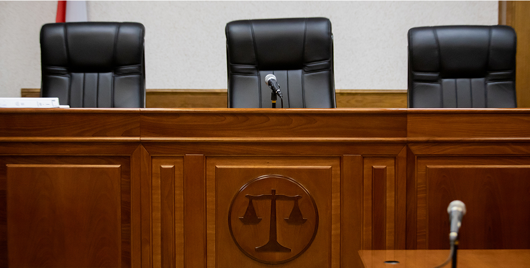 Three black leather chairs behind the wooden bench in a court room.