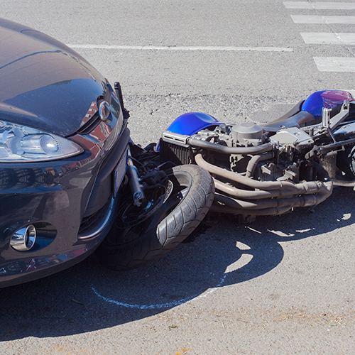 A motorcycle lying in the road under a car after a wreck.