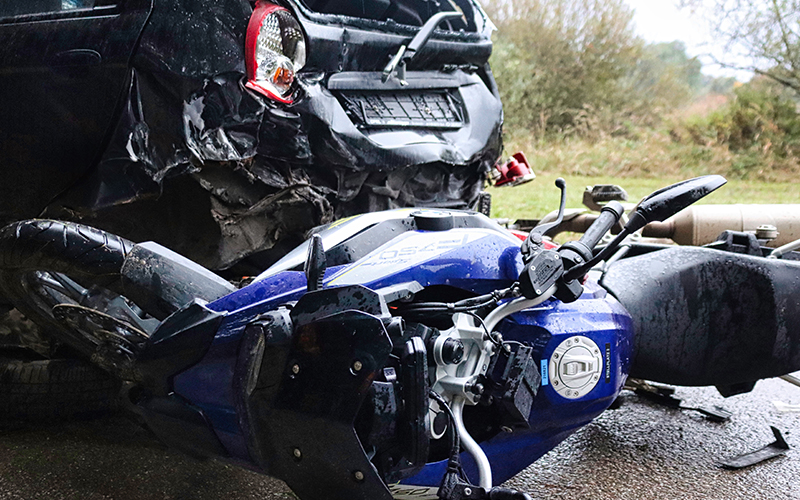 Wreckage from a traffic accident involving a blue motorcycle and a black car on a wet road.