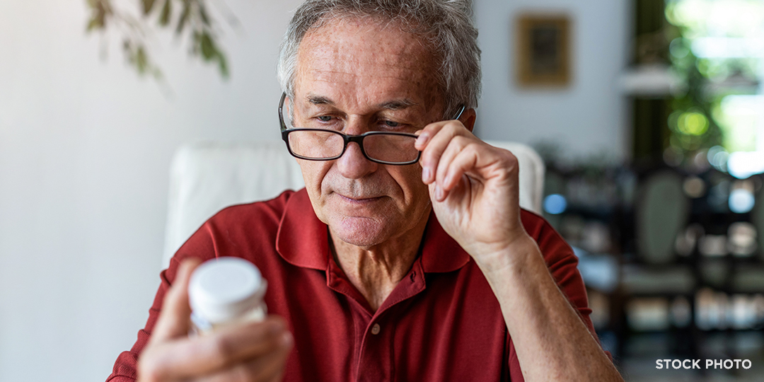 Older man adjusting his glasses to read the label on a medicine bottle.