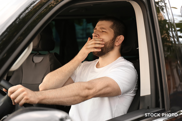 A drowsy young man yawning behind the wheel of his car.