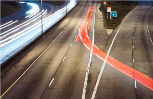 Trailing brake lights of a car crossing multiple lanes on a highway at night.