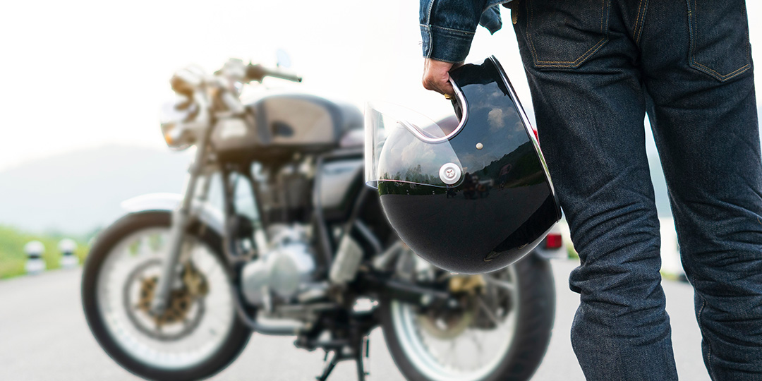 Motorcycle rider walking to his bike holding his helmet in his hand.