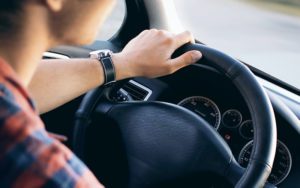 A person driving a car with their hand on the steering wheel.