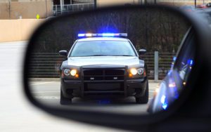 A police car with lights on seen in the side view mirror of a car.