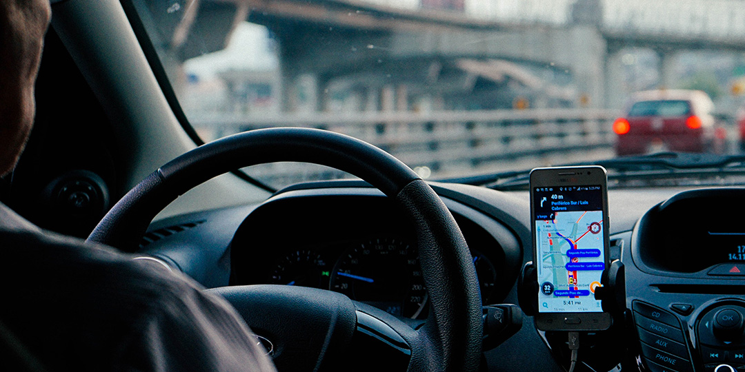 A rideshare driver behind the wheel with his phone on the dashboard of his car.