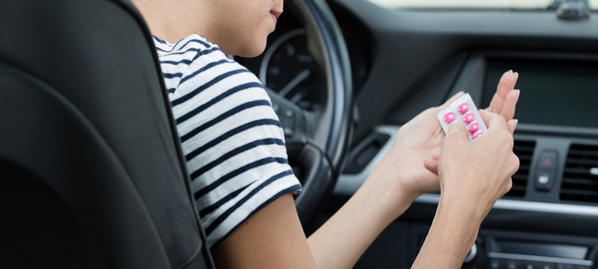 Driver taking benadryl pills while in the car.