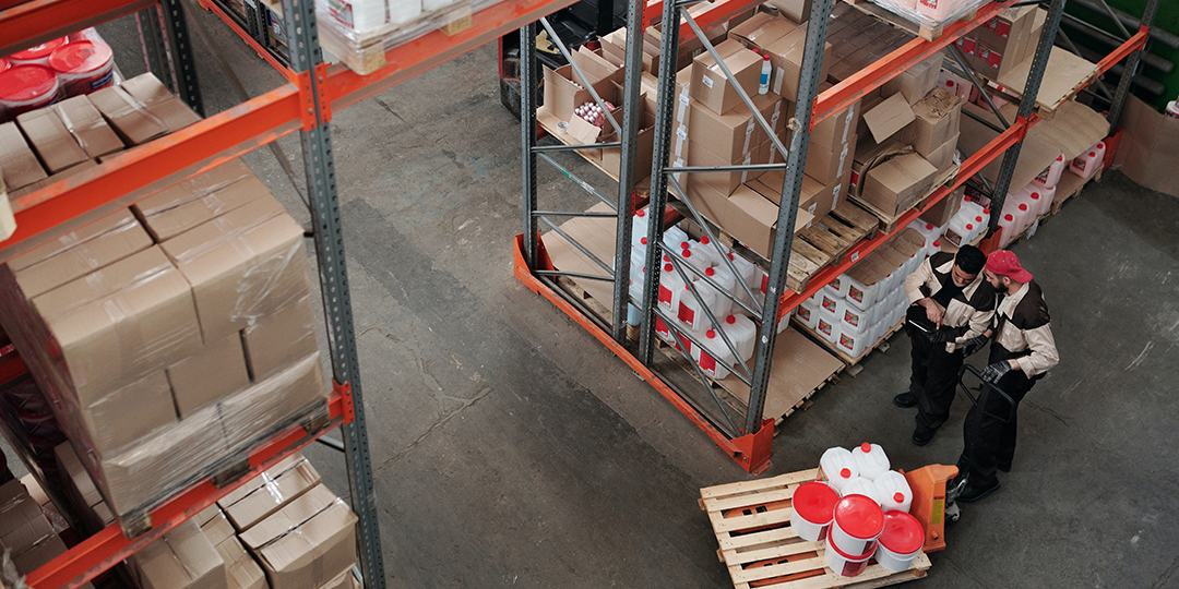 Two workers with a pallet of product in a large warehouse, seen from above.