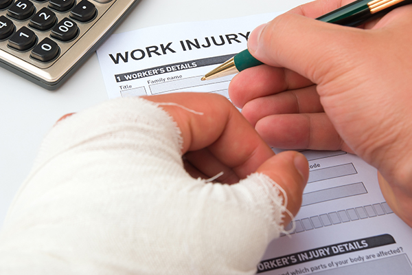 Close up of a worker with a bandaged injured hand filling out a workers' compensation report.