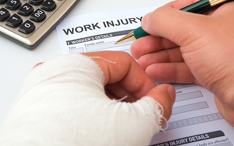 Close up of a worker with a bandaged injured hand filling out a workers' compensation report.