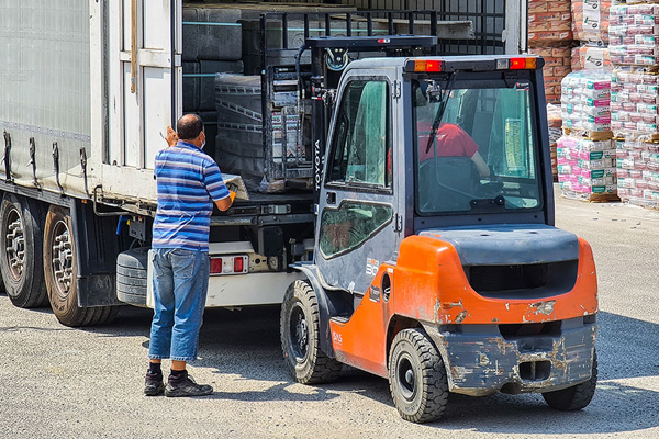A forklift operator unloading a semi truck while a worker supervises